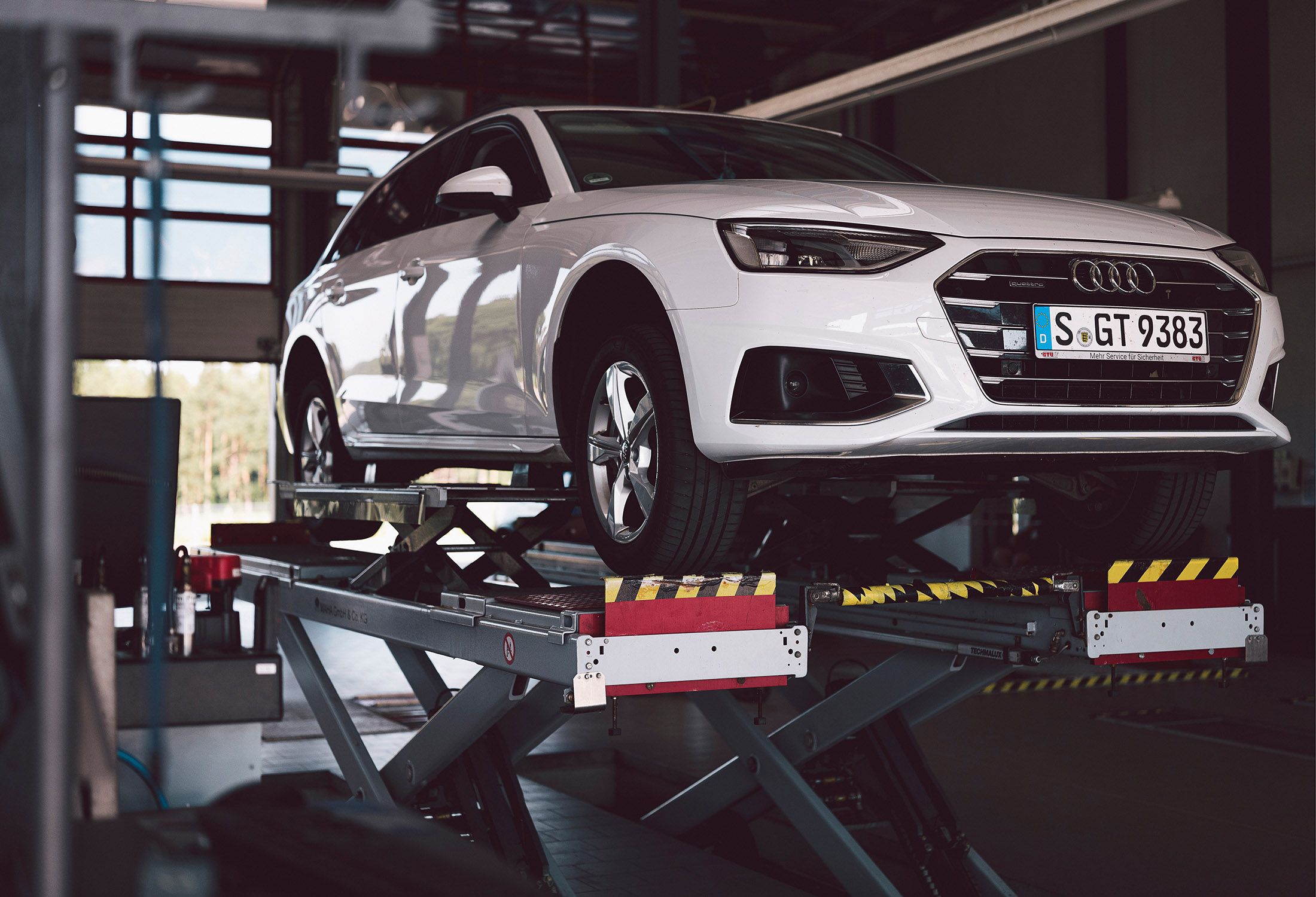 Weißer Audi steht auf einer Hebebühne in einer Werkstatt.