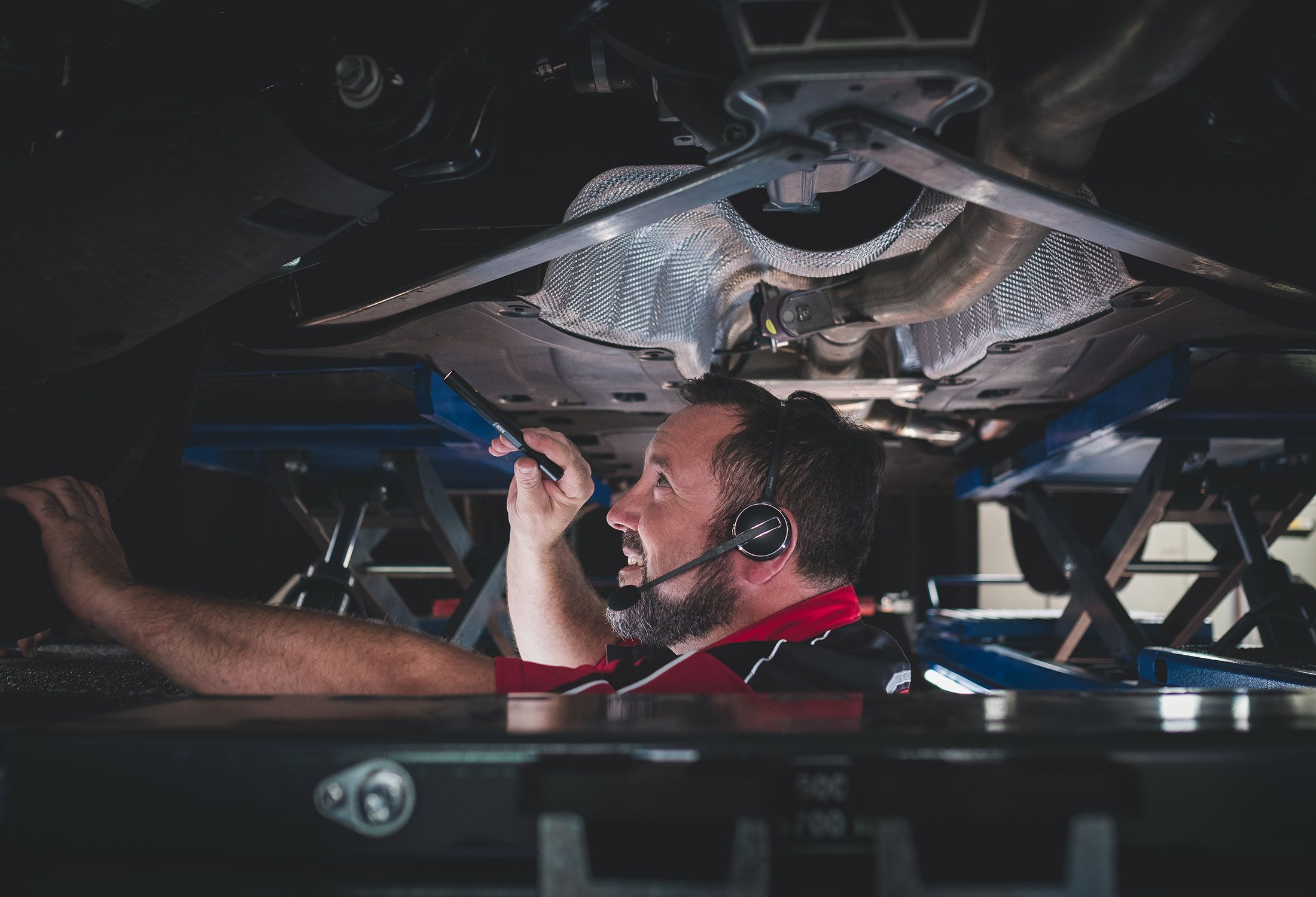 Kfz-Prüfingenieur untersucht mithilfe einer Taschenlampe den Motor eines Fahrzeugs.