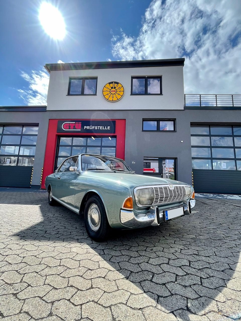 Oldtimer steht vor einer GTÜ-Prüfstelle unter sonnigem Himmel.