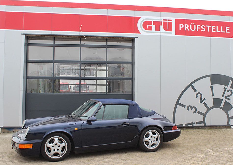 Seitenansicht eines dunkelblauen Porsche Oldtimers, der vor einer GTÜ-Prüfstelle steht.